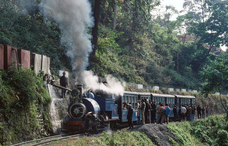 Darjeeling Himalayan Railway narrow gauge steam locomotive, class B 0-4-0ST no. 795 taking water while heading up the mountain to Darjeeling with a passenger train, India,